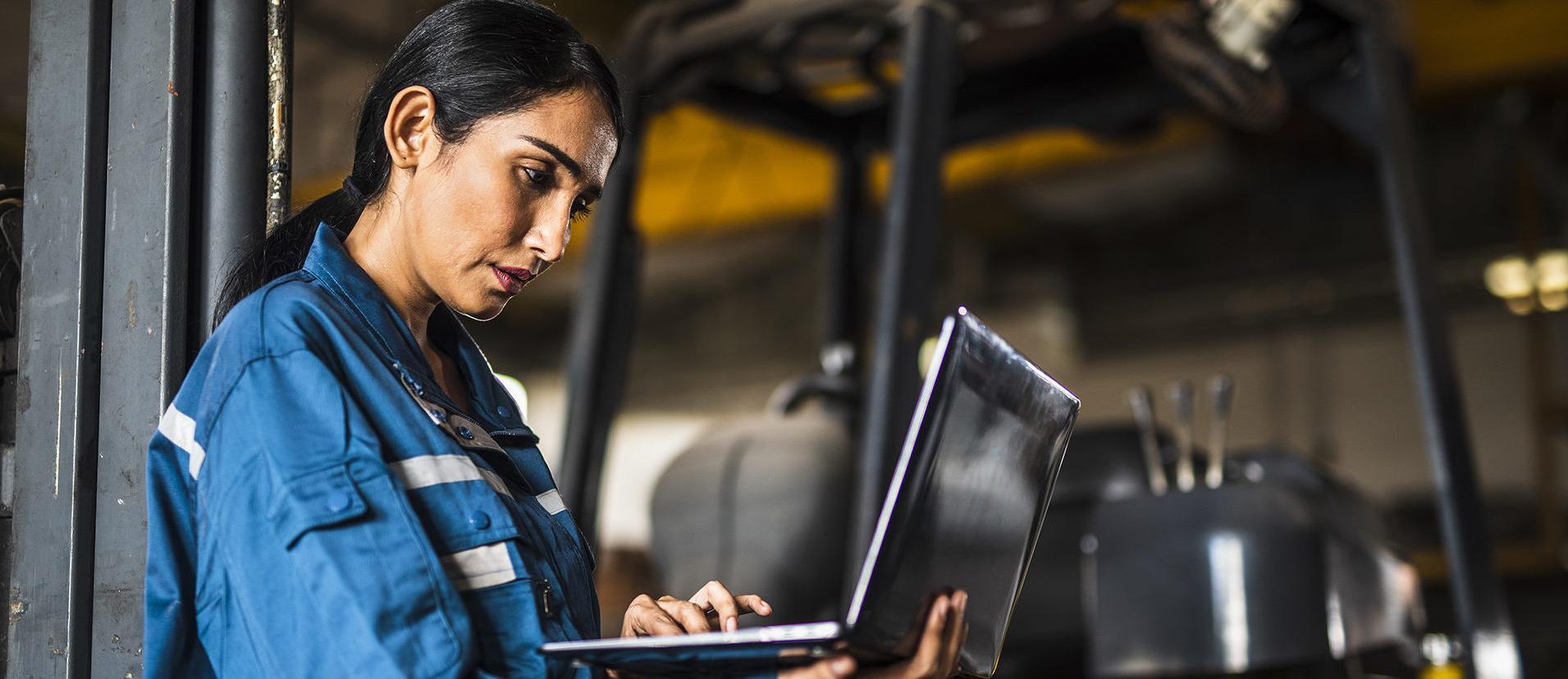 Indian Female Steel Factory Worker using a laptop in front of forklift