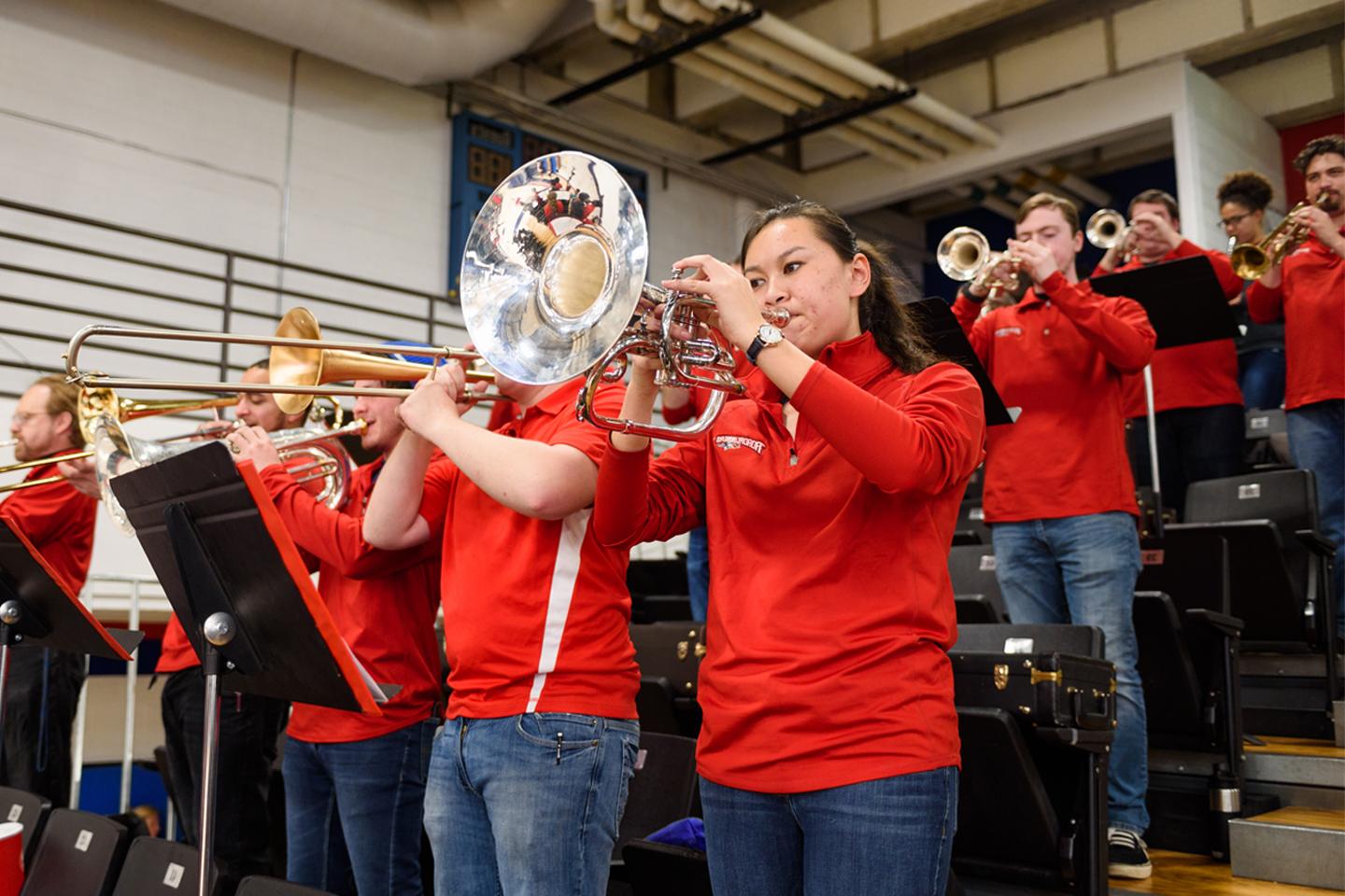 Group of pep band musicians in red playing in a basketball court