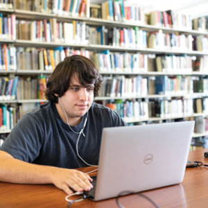 A student sitting in a library working on a laptop